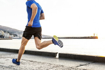 back male runner running embankment in sunrise, jogging along pier in background rising sun and...