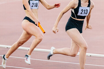 women running relay race in summer athletics championship, passing baton two female athletes