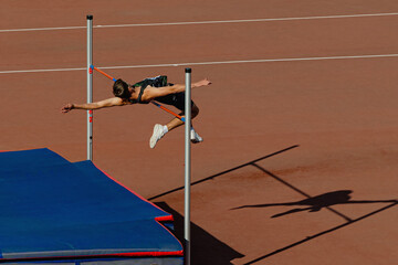 athlete jumper high jump in summer athletics competition, silhouette high jumper on red track stadium