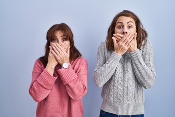 Mother and daughter standing over blue background shocked covering mouth with hands for mistake....