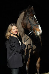 Beautiful woman with dressage horse in dark stable 