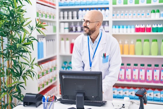 Young bald man pharmacist smiling confident using computer at pharmacy