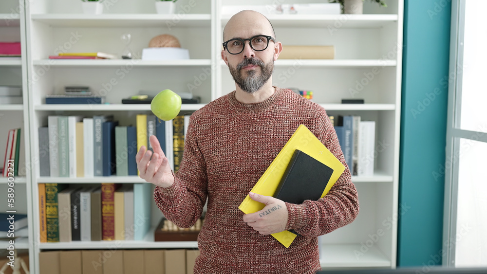 Wall mural Young bald man teacher holding books and apple at university classroom