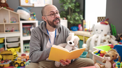 Young bald man preschool teacher reading story book at kindergarten