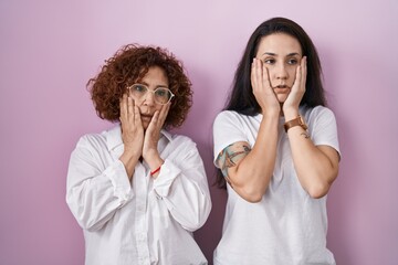 Hispanic mother and daughter wearing casual white t shirt over pink background tired hands covering face, depression and sadness, upset and irritated for problem