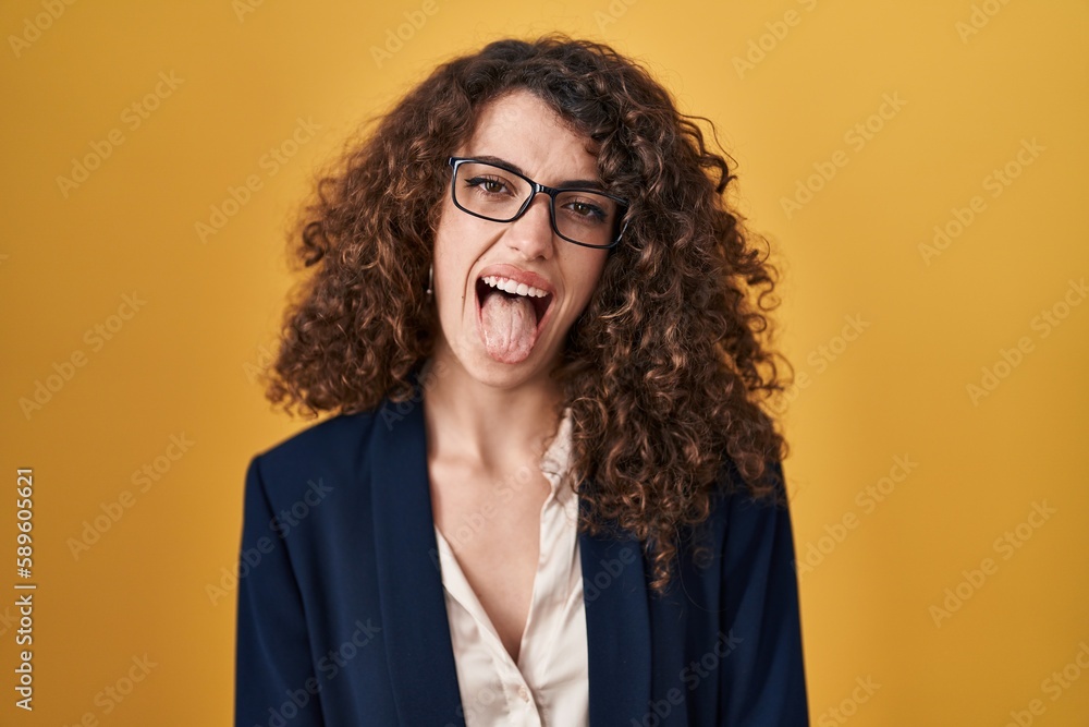 Sticker Hispanic woman with curly hair standing over yellow background sticking tongue out happy with funny expression. emotion concept.