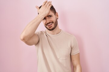Hispanic man with beard standing over pink background surprised with hand on head for mistake,...