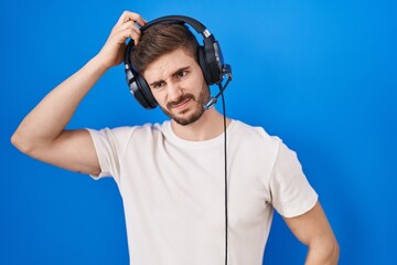 Hispanic man with beard listening to music wearing headphones confuse and wondering about question. uncertain with doubt, thinking with hand on head. pensive concept.