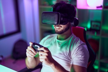 Young hispanic man streamer using virtual reality glasses playing video game at gamin room