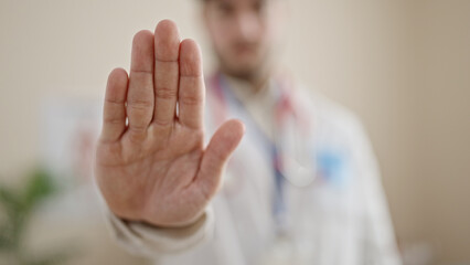 Young hispanic man doctor doing stop sign with hand at clinic
