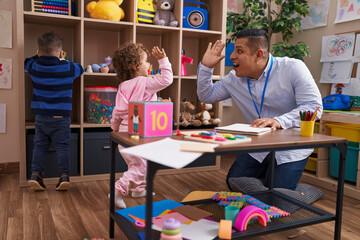 Hispanic man and girl high five with hands raised up at kindergarten