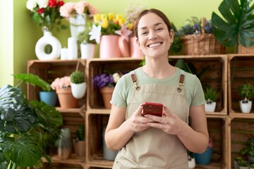 Young beautiful woman florist smiling confident using smartphone at flower shop