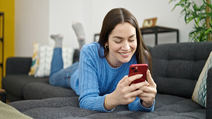 Young caucasian woman using smartphone lying on sofa at home