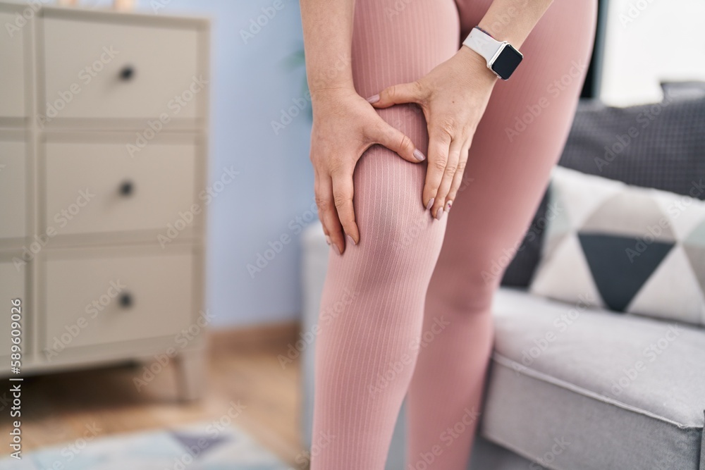 Wall mural young woman wearing sportswear touching injured knee at home