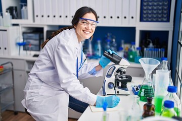 Young woman scientist writing on notebook using microscope at laboratory