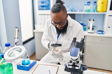 Young african american man wearing scientist uniform using loupe at laboratory