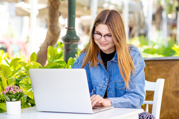 Young woman, digital nomad working remotely from a cafe, drinking coffee and using laptop, smiling. 