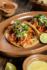 delicious al pastor beef tacos with cilantro and onion on a clay plate accompanied by green and red sauce