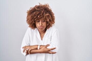 Young hispanic woman with curly hair standing over white background shaking and freezing for winter...