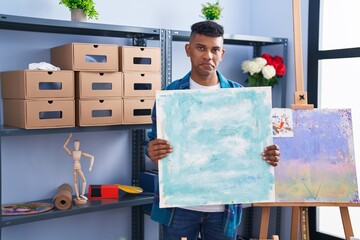 Young hispanic man holding canvas at artist studio depressed and worry for distress, crying angry...