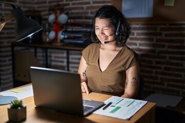 Young hispanic woman working at the office at night winking looking at the camera with sexy...
