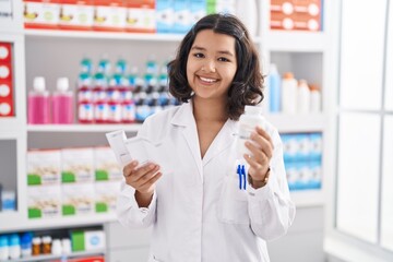 Young woman pharmacist holding pills bottle reading prescription at pharmacy