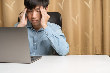 Young Asian Business man with long business shirt is do Migraine massage to cure headache, stress, office syndrome treatment when work from home on laptop at home office. Office syndrome concept.