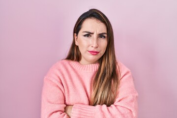 Fototapeta premium Young hispanic woman standing over pink background skeptic and nervous, disapproving expression on face with crossed arms. negative person.