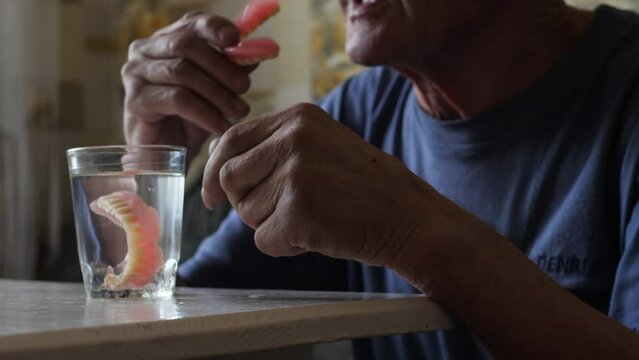 pensioner takes out of a glass and puts on removable dentures, lifestyle of the elderly, loss of teeth in old age, implantation, care for removable teeth, dentures