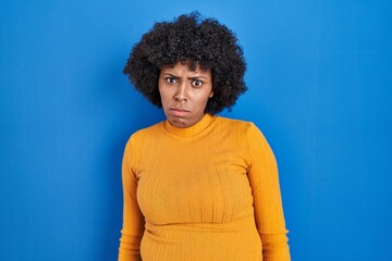 Fototapeta na wymiar Black woman with curly hair standing over blue background skeptic and nervous, frowning upset because of problem. negative person.