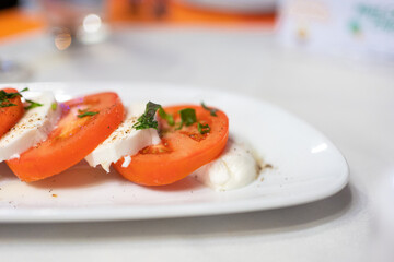 Caprese Salad with Mozzarella cheese, tomatoes, basil, olive oil on white plate at Italian diner, restaurant. Close up fresh Caprese is traditional Italian food from Italy. Traditional food concept.