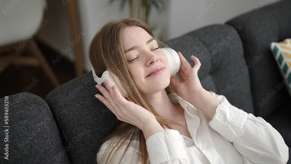 Wall mural young blonde woman listening to music sitting on sofa at home