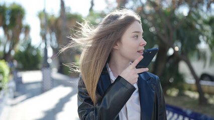 Young blonde woman sending voice message with smartphone at park