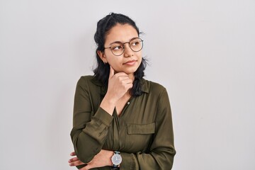 Hispanic woman with dark hair standing over isolated background with hand on chin thinking about question, pensive expression. smiling with thoughtful face. doubt concept.