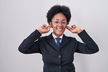 Beautiful african woman with curly hair wearing business jacket and glasses smiling pulling ears...