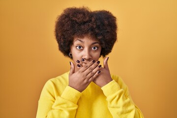 Fototapeta na wymiar Young african american woman standing over yellow background shocked covering mouth with hands for mistake. secret concept.