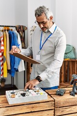 Middle age grey-haired man shop assistant writing on document looking watch at clothing store