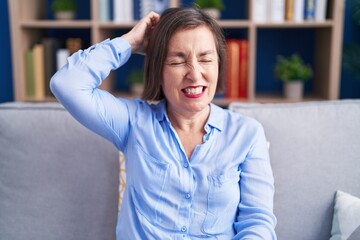 Middle age hispanic woman sitting on the sofa at home confuse and wonder about question. uncertain with doubt, thinking with hand on head. pensive concept.