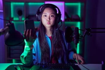 Young asian woman playing video games with smartphone puffing cheeks with funny face. mouth inflated with air, crazy expression.