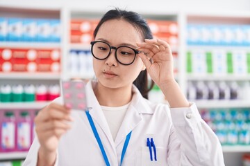 Young chinese woman pharmacist smiling confident holding pills tablet at pharmacy