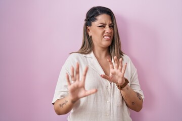 Blonde woman standing over pink background disgusted expression, displeased and fearful doing...