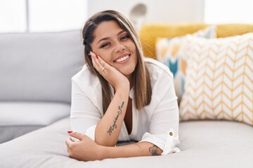 Young hispanic woman smiling confident lying on sofa at home