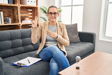 Young woman working at consultation office smiling swearing with hand on chest and fingers up,...