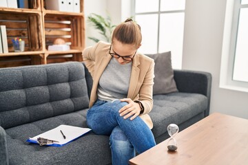 Fototapeta premium Young woman working at consultation office suffering of backache, touching back with hand, muscular pain
