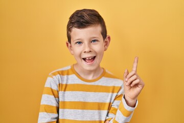Young caucasian kid standing over yellow background with a big smile on face, pointing with hand and finger to the side looking at the camera.