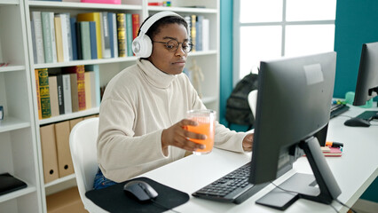 Fototapeta na wymiar African american woman student using computer and headphones drinking orange juice at library university