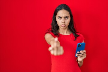 Young brazilian woman using smartphone over red background showing middle finger, impolite and rude...