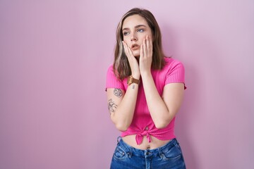 Blonde caucasian woman standing over pink background tired hands covering face, depression and sadness, upset and irritated for problem