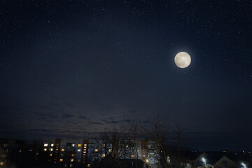 Full moon in dark star sky over town roofs.