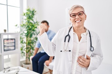 Female doctor wearing uniform and stethoscope at medical clinic pointing thumb up to the side smiling happy with open mouth